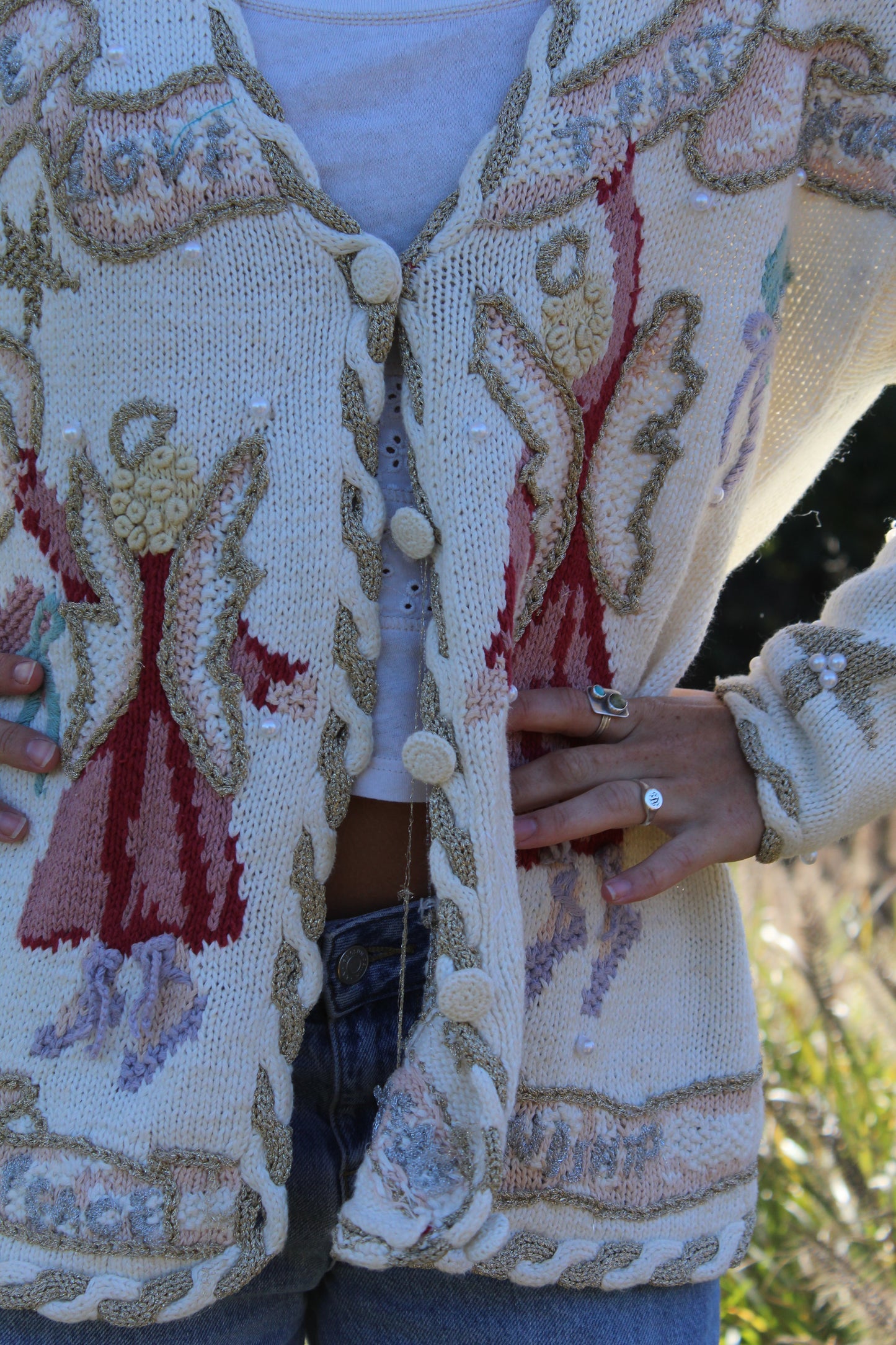 “Unique white button-up sweater with whimsical angel details, hand-stitched embroidery, and beaded embellishments.”