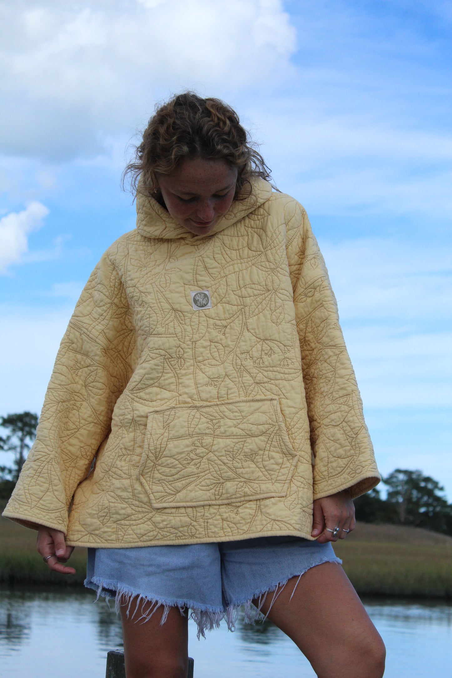 close up of quilted yellow hoodie and floral details with front pocket