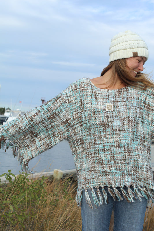 Person wearing a patterned poncho and jeans standing outdoors with a clear blue sky.