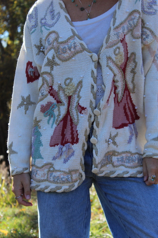 “Close-up of a vintage-style white sweater with angel motifs, hand embroidery, and subtle bead accents.”