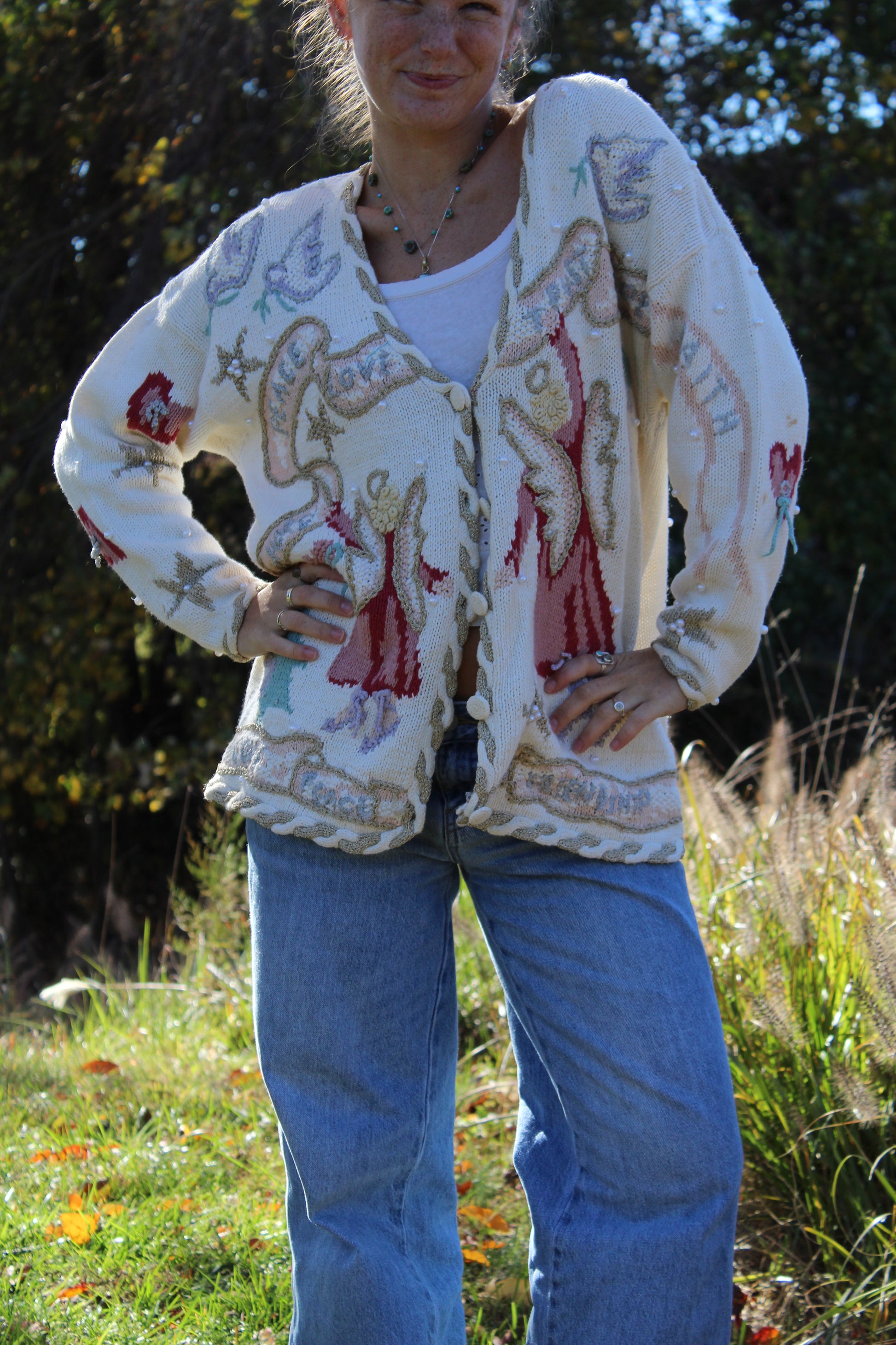 “Hand-embellished white sweater with angel illustrations, beadwork, and intricate stitched detailing.”