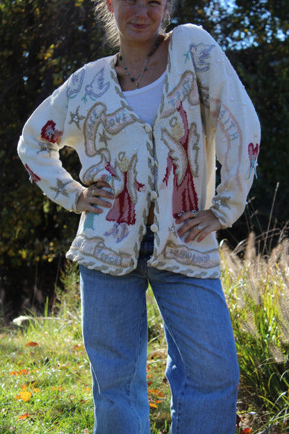 “Hand-embellished white sweater with angel illustrations, beadwork, and intricate stitched detailing.”