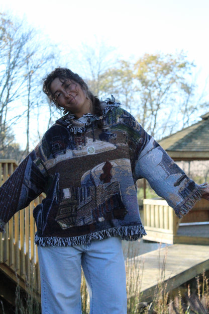 Fringed blanket hoodie featuring artistic woven designs and a relaxed boho feel.