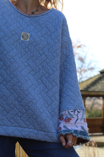 Sustainable upcycled crewneck in quilted blue fabric with decorative floral fringe cuffs.