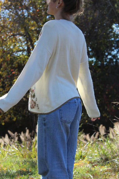 Close-up of a sweater with floral embroidery, gold edging, and button closure.