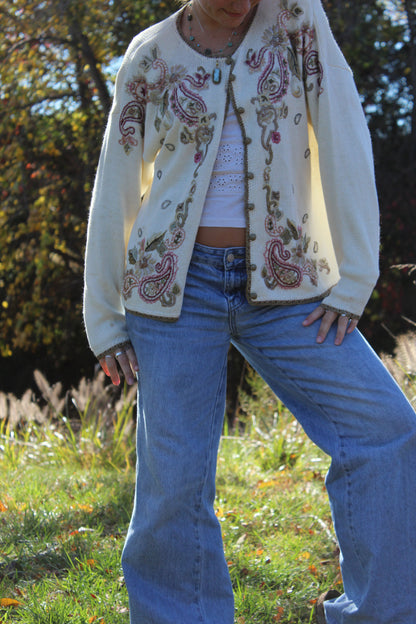Soft knit sweater decorated with floral embroidery, gold accents, and buttons down the front.