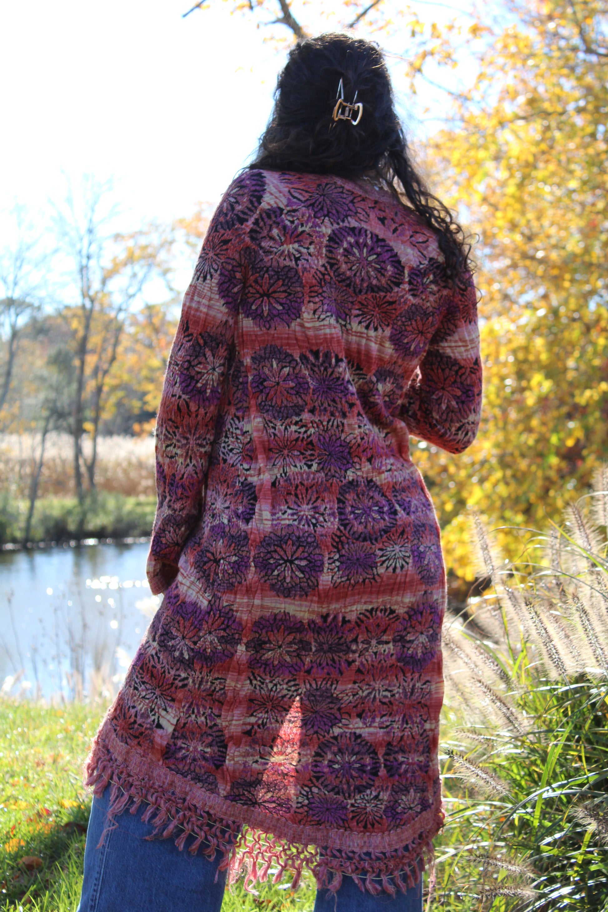 Close-up of a red and purple floral sweater with fringe trim and clasp closure.