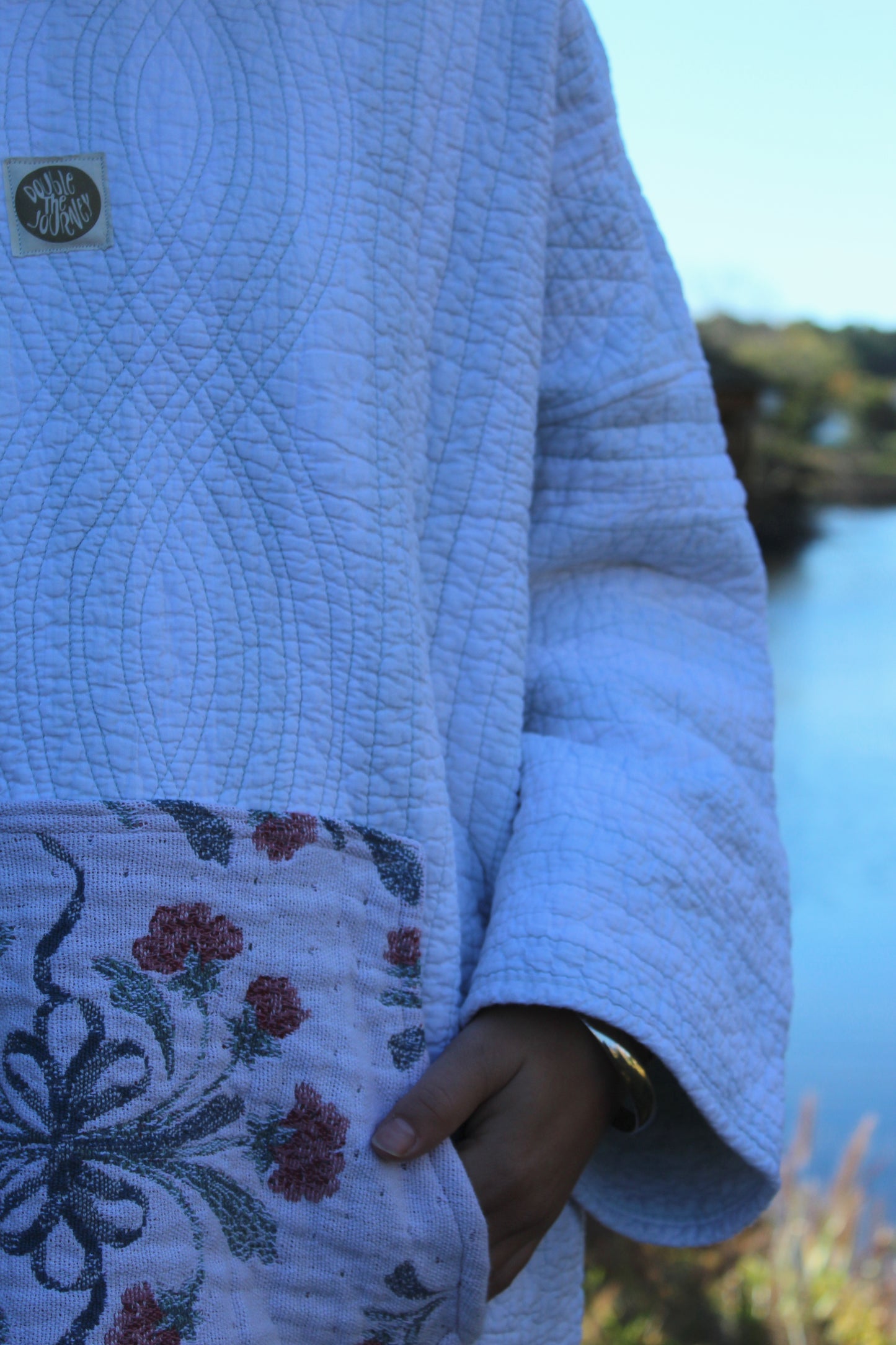 Upcycled quilted hoodie with blue striped panels and a charming floral patch pocket.