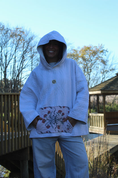 Handcrafted quilted hoodie featuring subtle blue striped fabric and a floral accent pocket.