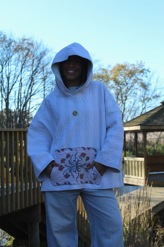 Handcrafted quilted hoodie featuring subtle blue striped fabric and a floral accent pocket.